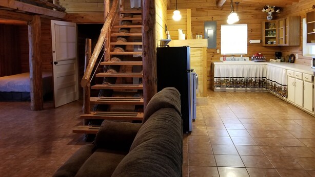 L’intérieur chaleureux d’un chalet avec un escalier en bois, un canapé, un coin cuisine et une table à manger.