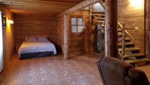 Une chambre située dans une cabane en rondins, avec un lit, un escalier en bois et un fauteuil en cuir marron.