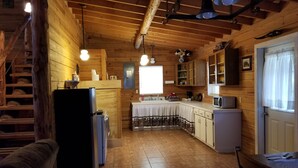 Une cuisine chaleureuse, aménagée dans le style d’un chalet, avec des murs en bois, un sol carrelé et un coin repas comprenant une table et des chaises.