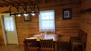 Une salle à manger en bois avec une table dressée pour quatre personnes, des chaises, un lustre et une fenêtre avec des rideaux.