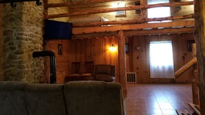 Un intérieur rustique avec des éléments en bois, un mur en pierre, un plafond en bois, un canapé, une cheminée et un escalier.