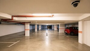 Een parkeergarage met betonnen vloeren, witte pilaren en rood gestreepte veiligheidsmarkeringen.