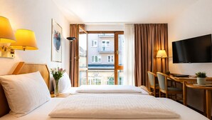 Een hotelkamer met een bed, een bureau, een televisie en uitzicht op gebouwen door een raam.