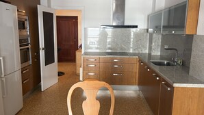 Een keuken met houten kastjes, een roestvrijstalen afzuigkap, een granieten aanrecht en een houten stoel.