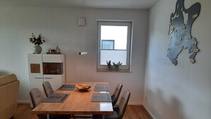 A dining area with a wooden table, four chairs, and a window with blinds. - Modern top floor apartment with a view of the sea and Stralsund (Altefähr)