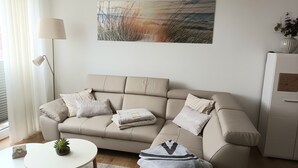 A modern living room with a beige sofa, a small white table, a floor lamp, and a painting on the wall. - Modern top floor apartment with a view of the sea and Stralsund (Altefähr)