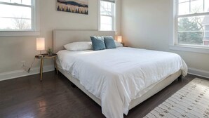 Un dormitorio con una cama grande, dos lámparas de noche, un cuadro en la pared y ventanas amplias.