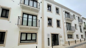 Un immeuble à plusieurs étages doté de balcons, avec une entrée au rez-de-chaussée, et une rue pavée.