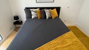 Une chambre à coucher avec un lit, une œuvre d’art murale et une petite table avec une lampe.