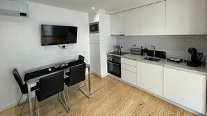 Une cuisine moderne avec des armoires blanches, un four à micro-ondes encastré, une cuisinière et un évier. On y trouve également un coin repas avec une table et des chaises.
