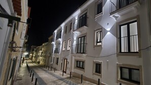 Une rue étroite bordée d’immeubles à étages, avec des balcons et des fenêtres illuminées.