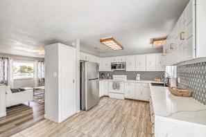 Una cocina moderna con armarios blancos, un refrigerador de acero inoxidable, un microondas y un salpicadero decorativo.