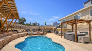 A swimming pool with lounge chairs and a hot tub in a backyard setting.