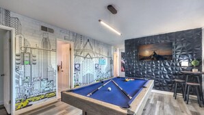 A pool table in a room with a cityscape mural and a geometric wall design.