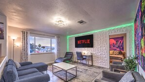 A modern living room with a large window, a flat-screen TV, a sofa, a coffee table, and a desk with a chair.