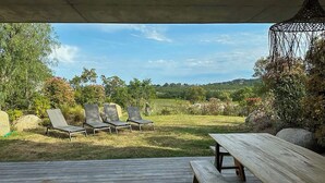 Un espace extérieur aménagé avec quatre fauteuils confortables et une table en bois, entouré de verdure et de rochers.