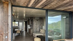 Un intérieur moderne avec un plafond en bois, une porte coulissante en verre donnant sur un balcon et un coin repas comprenant une table et des chaises.