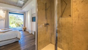 Une salle de bain moderne avec une douche en verre, un grand lit donnant sur l’extérieur et un plancher en bois.