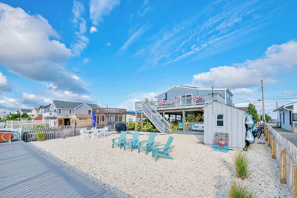 A beachfront property with a wooden deck, outdoor seating, and a building with a staircase leading to a deck.