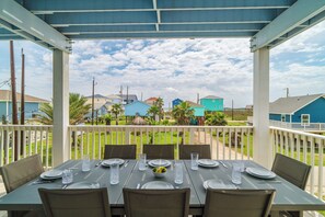 Un espace de restauration extérieur abrité, avec des tables disposées pour accueillir quatre personnes, offrant une vue sur un quartier résidentiel avec ses maisons et ses palmiers.