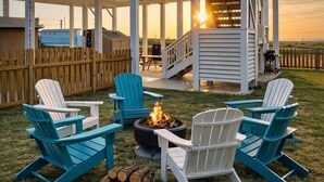 An outdoor seating area with Adirondack chairs and a fire pit, surrounded by a wooden fence and a covered structure. - Steps to Surfside Beach | Games, Views & Pets (Surfside Beach)