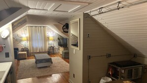 Een slaapkamer in loft-stijl met een houten vloer, een bed, een bureau en een televisie.