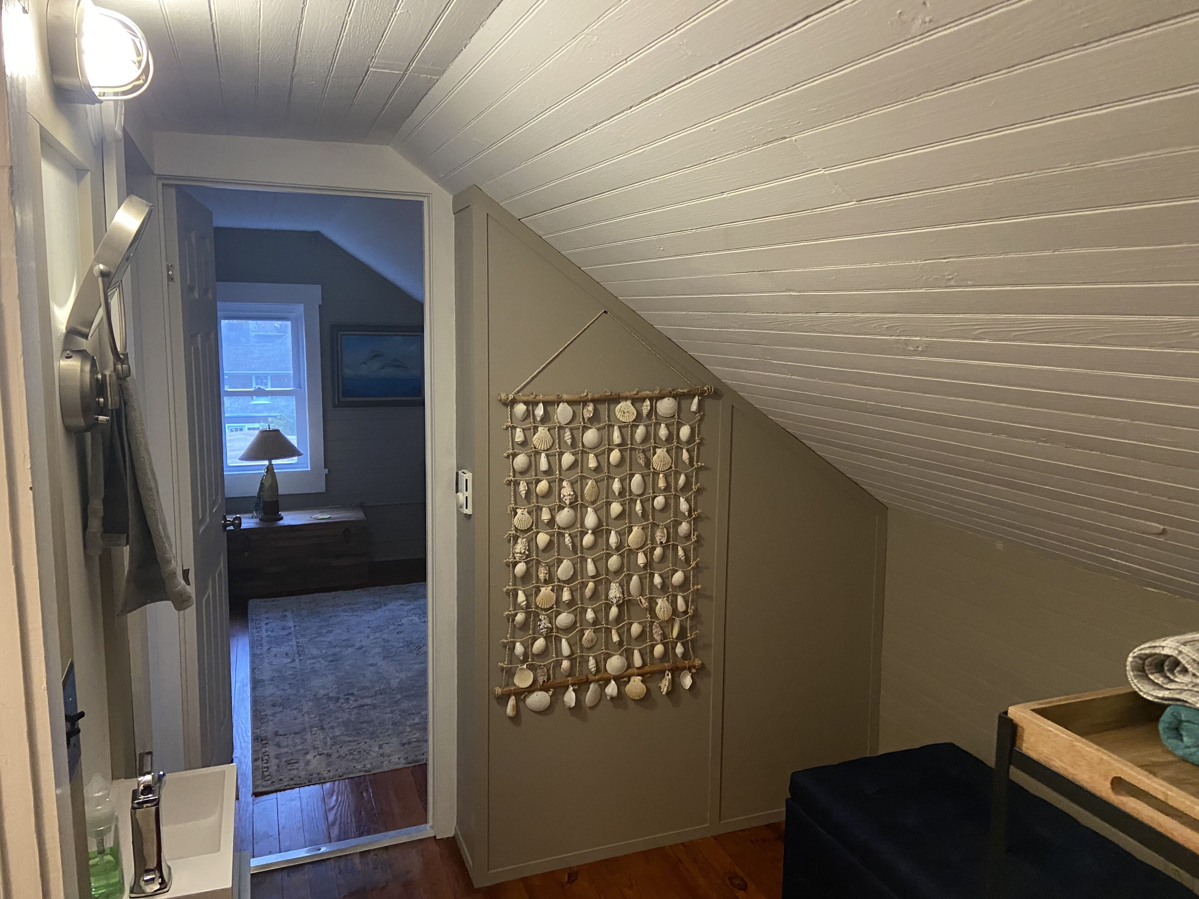 Ein Zimmer mit schrägem Dach, einer Tür mit Spiegel und einer Wanddekoration in Form einer Muschel, sowie eine Holzbank.