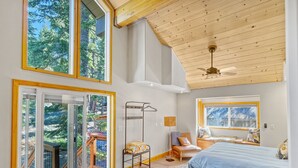 A spacious bedroom with a large bed, a view of the outdoors through a sliding glass door, a ceiling fan, and a wooden ceiling. - Lake Views, Hot Tub, Walk to Beach! (Carnelian Bay)