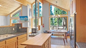A modern kitchen with wooden cabinets, a granite countertop, and a large island. There are multiple windows providing natural light and views of the outdoors. - Lake Views, Hot Tub, Walk to Beach! (Carnelian Bay)