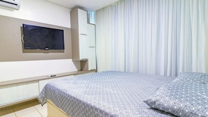 Hotellihuone, jossa on sänky, seinälle asennettu televisio, vaatekaappi ja ikkuna, jossa on verhot.
