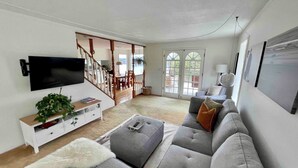 Una sala de estar moderna con un sofá gris, un televisor de pantalla plana y una escalera que lleva a un comedor.