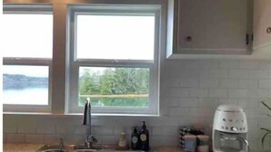 Una cocina con un lavamanos doble, una cafetera y vistas a un lago a través de dos ventanas.