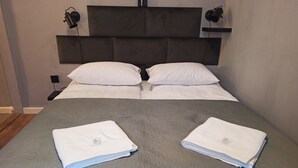 Ein ordentlich bezogenes Bett mit weißen Leinen und zwei gefalteten Handtüchern auf einer grauen Bettdecke.