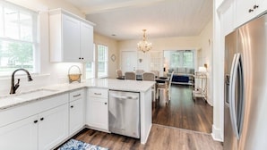 A modern kitchen with white cabinetry, a stainless steel dishwasher, and a large island. - Our Nest at Spiller l Adorable Home near UA (Tuscaloosa)