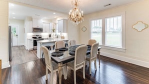 A spacious kitchen with white cabinets, a central island, and a dining area with a chandelier. - Our Nest at Spiller l Adorable Home near UA (Tuscaloosa)