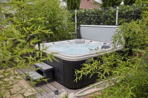 A hot tub in a garden setting with a wooden deck, surrounded by greenery and a metal fence. - Riverside boutique apartments next to the thermal bath (Mosonmagyaróvár)