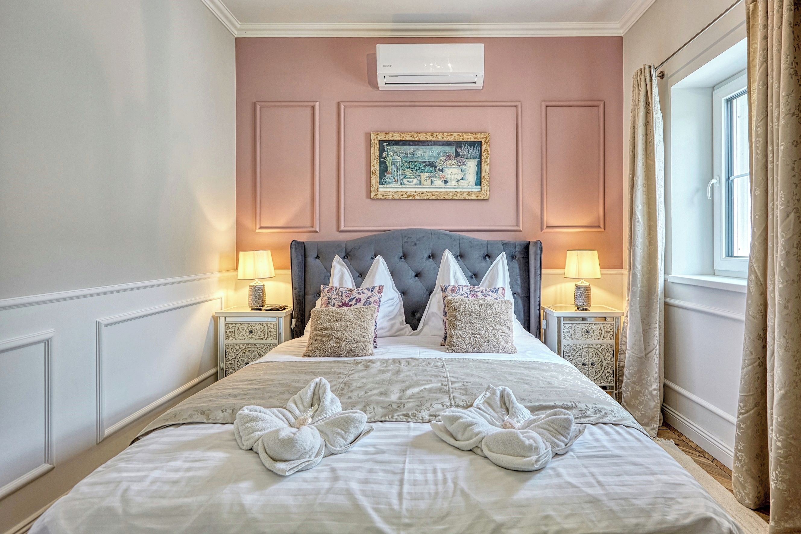 A hotel room with a large bed, two bedside lamps, a picture on the wall, and a window with curtains.