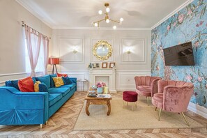 A living room with a blue sofa, a pink armchair, a wooden coffee table, and a fireplace. - Riverside boutique apartments next to the thermal bath (Mosonmagyaróvár)
