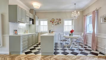 A modern kitchen with a central island, clear chairs, and a chandelier.