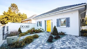 Valkoinen rakennus, jossa on keltainen ovi, siniset ikkunaluukut ja kyltti, jossa lukee: ”The Doors Boutique Apartments”.
