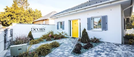 A white building with a yellow door, blue shutters, and a sign reading "The Doors Boutique Apartments."