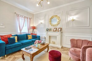 A living room with a blue sofa, a red ottoman, a wooden coffee table, and a fireplace. - Riverside boutique apartments next to the thermal bath (Mosonmagyaróvár)
