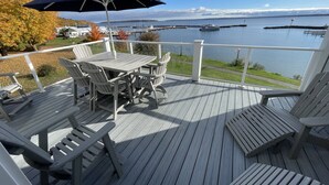 Een houten terras met buitenmeubilair, een tafel en stoelen, met uitzicht op een waterpartij met boten en steigers.