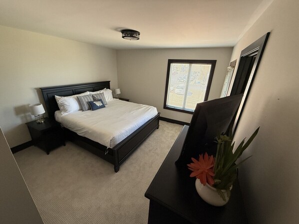 Habitación de hotel con cama, mesita de noche, escritorio con planta y ventana con persianas.