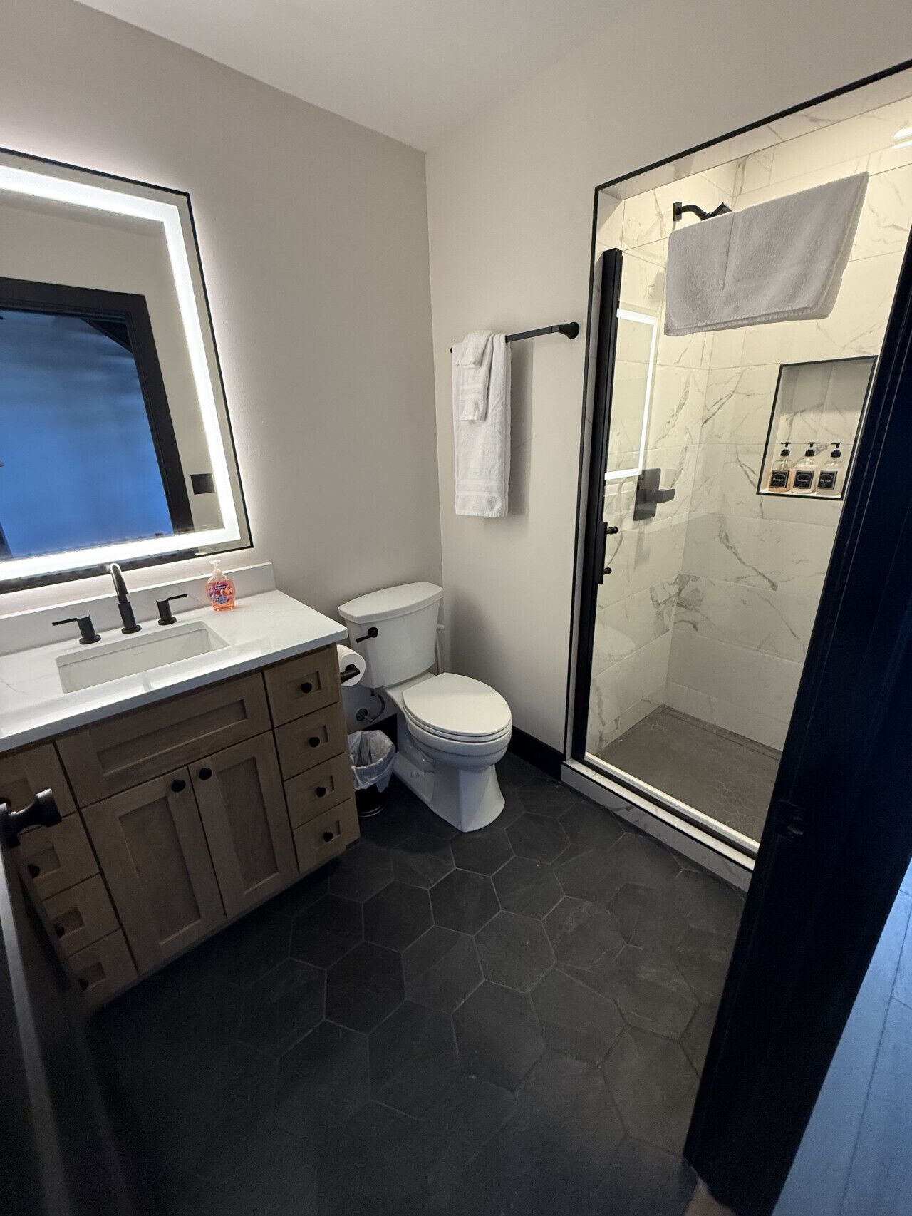 Une salle de bain moderne avec une douche à parois de verre, des toilettes blanches et un meuble-lavabo doté d’un miroir et d’un évier.