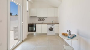 A compact kitchen with a washing machine, oven, and a small table with tea cups and cookies.