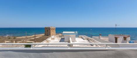 A coastal view with a clear sky, a tower, and a building with a flat roof.