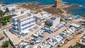 Vista aérea de un pueblo costero con edificios modernos, una torre histórica y un puerto deportivo con barcos.