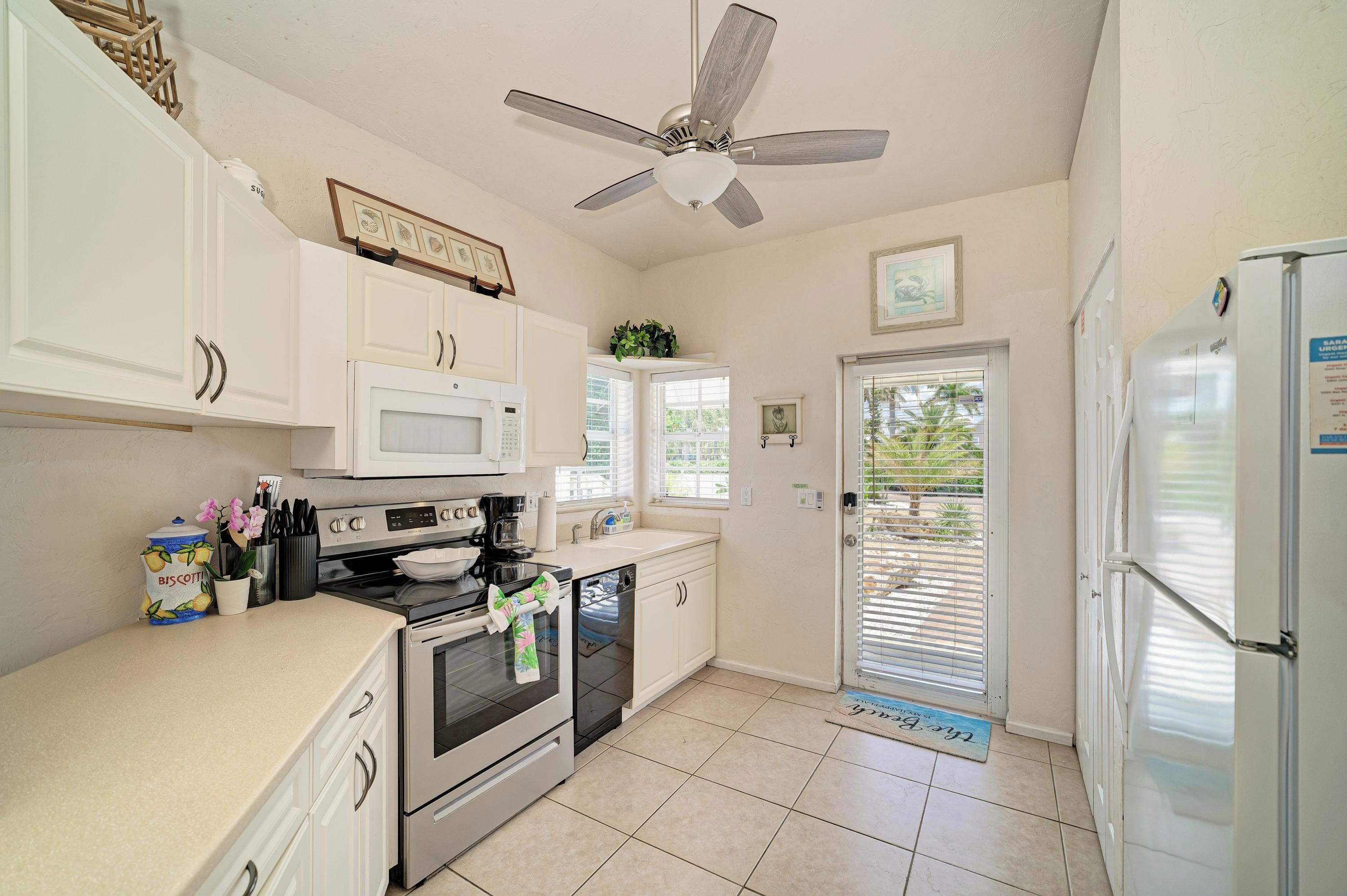 A kitchen with white cabinets, a microwave, an oven, a coffee maker, and a ceiling fan.