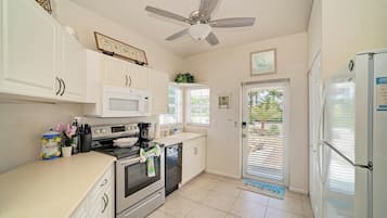 A kitchen with white cabinets, a microwave, an oven, a coffee maker, and a ceiling fan.